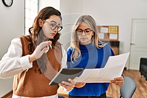 Two business workers woman reading paperwork using touchpad at the office