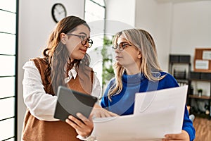 Two business workers woman reading paperwork using touchpad at the office