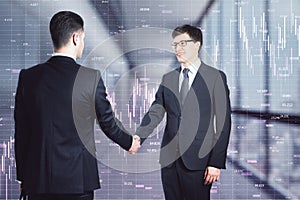 Two businessman making a deal, shaking hands in the office corridor and market charts in the background. Agreement and partnership