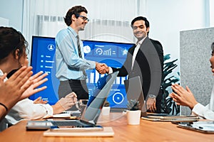 Two businessman shake hand in meeting room with cheerful colleagues. Habiliment