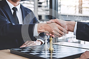 Two Businessman shaking hands after end playing chess game reaching plan for success, thinking overcoming difficulty and achieving