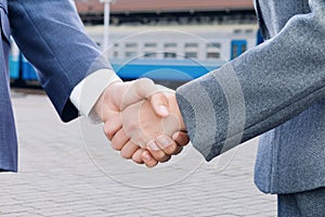 Two businessman are shaking their hands at the overhead railway background. The concept is the interaction of different business