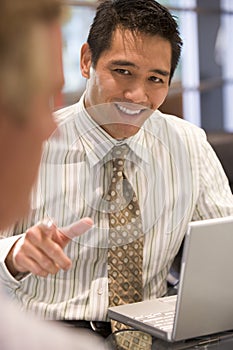 Two businessmen in boardroom with laptop talking