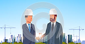 Two businessmen builders handshake agreement during meeting over city construction site tower cranes building