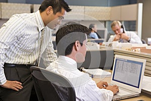 Two businessmen in cubicle looking at laptop