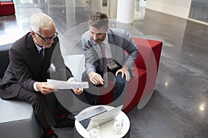 Two Businessmen Discuss Document In Lobby Of Modern Office