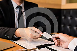 Two businessmen exchanged white business cards on a wooden table in office