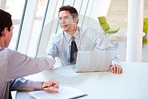 Two Businessmen Having Meeting Around Table In Modern Office