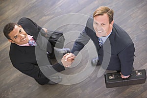 Two businessmen indoors shaking hands smiling