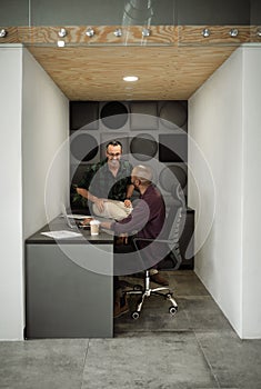 Two businessmen laughing while working together in an office cubicle