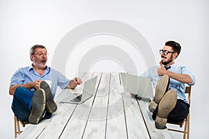 The two businessmen with legs over table working on laptops