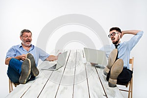 The two businessmen with legs over table working on laptops