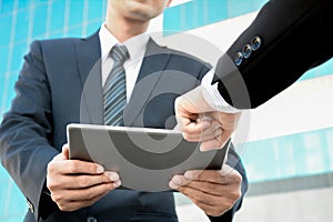 Two businessmen looking at tablet computer with one hand pointing screen