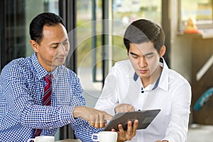 Two businessmen meeting in coffee shop watching business plan presentation in tablet
