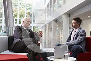 Two Businessmen Meeting In Lobby Area Of Modern Office