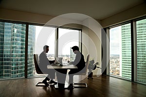 Two businessmen negotiating sitting at conference table in moder