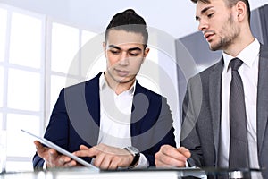 Two businessmen or partners working with tablet computer at the desk in modern office. Headshot of arab male