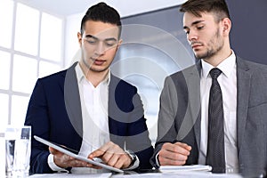 Two businessmen or partners working with tablet computer at the desk in modern office. Headshot of arab male