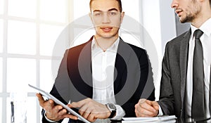 Two businessmen and partners working with tablet computer at the desk in sunny office. Multi ethnic teamwork