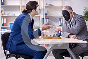 Two businessmen playing chess wearing masks