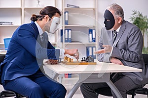Two businessmen playing chess wearing masks