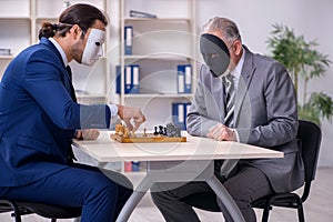 Two businessmen playing chess wearing masks