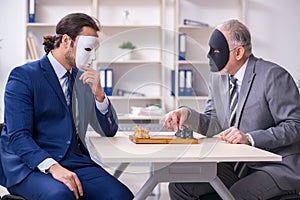 Two businessmen playing chess wearing masks