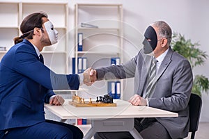 Two businessmen playing chess wearing masks