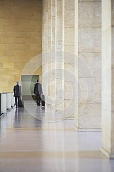 Two Businessmen Pulling Luggage In Airport Lobby