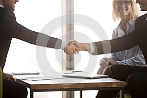 Satisfied business partners in suits shake hands, close up view