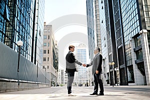 Two businessmen shaking hands on background office corporate buildings