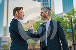 Two businessmen shaking hands on city street. Business men in suit shaking hands outdoors. Handshake between two