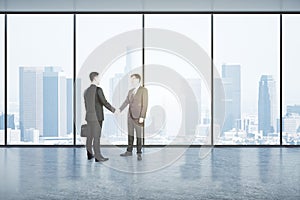 Two businessmen shaking hands in an empty big office room with big windows and city view, reaching an agreement. Communication and