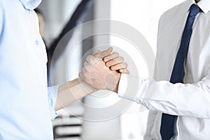 Two businessmen are shaking hands in office, close-up. Happy and excited business woman stands with raising hands at the