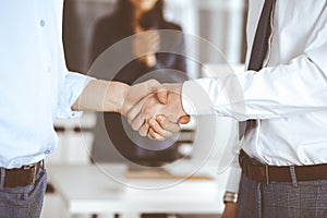 Two businessmen are shaking hands in office, close-up. Happy and excited business woman stands with raising hands at the