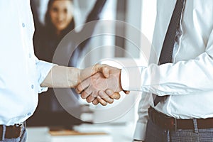 Two businessmen are shaking hands in office, close-up. Happy and excited business woman stands with raising hands at the