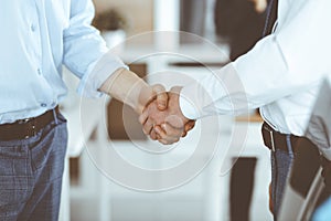 Two businessmen are shaking hands in office, close-up. Happy and excited business woman stands with raising hands at the