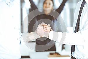 Two businessmen are shaking hands in office, close-up. Happy and excited business woman stands with raising hands at the