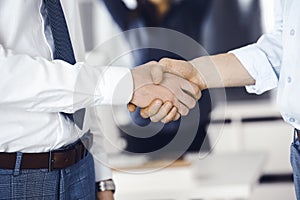 Two businessmen are shaking hands in office, close-up. Happy and excited business woman stands with raising hands at the