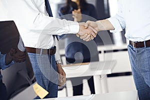 Two businessmen are shaking hands in office, close-up. Happy and excited business woman stands with raising hands at the