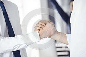 Two businessmen are shaking hands in office, close-up. Happy and excited business woman stands with raising hands at the