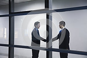 Two businessmen shaking hands, seen through glass wall