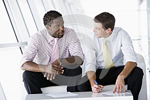 Two businessmen sitting in office lobby talking