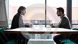 Two businessmen sitting opposite at table, confrontation and negotiation