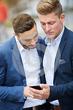 Two businessmen standing outside and looking at phone
