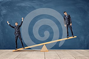 Two businessmen standing on a wooden seesaw, one happy and one sad looking. photo