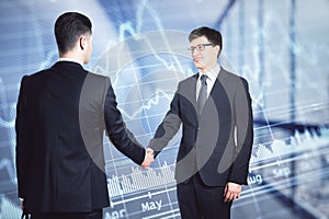 Two businessmen in suits shaking hands on the background of financial chart in office.