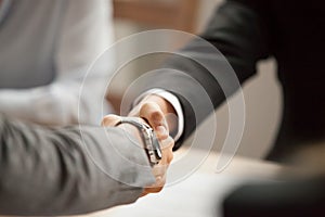 Two businessmen in suits shaking hands at meeting, close up