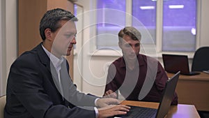 Two businessmen at a table in front of a laptop