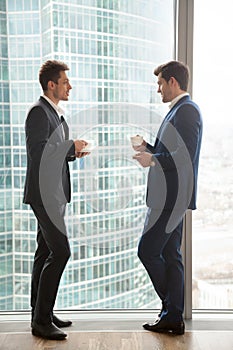 Two businessmen talking, having coffee break, standing near full